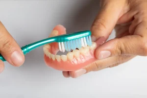 Hands holding dentures and brushing them with a tooth brush,